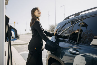 Smiling businesswoman charging electric car at charging station