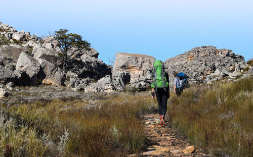 Rear view of hikers walking on mountain against clear sky