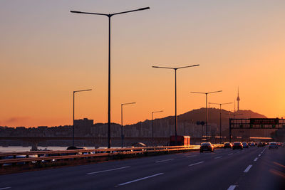 Cars moving on road against clear sky at sunset