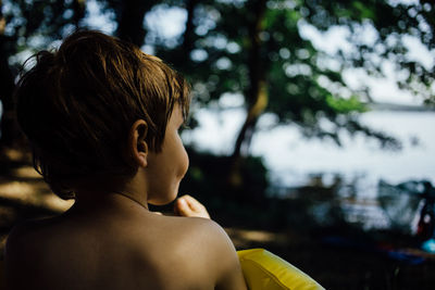 Rear view of shirtless boy at lakeshore