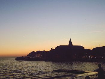 Silhouette church by sea against clear sky during sunset