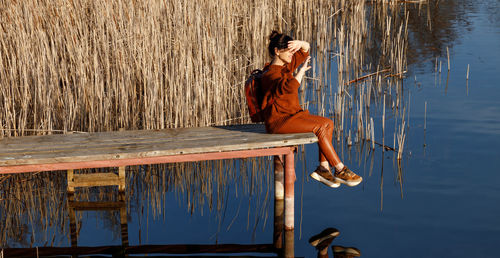 Side view of woman sitting on pier over lake