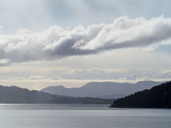 Scenic view of sea and mountains against cloudy sky