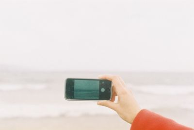 Hand photographing the sea with mobile phone