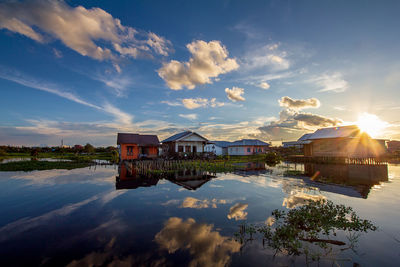 Houses by lake and buildings against sky during sunset