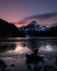 Scenic view of lake by snowcapped mountains against sky during sunset