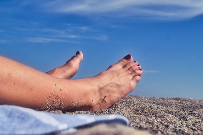 Low section of woman relaxing at beach against sky