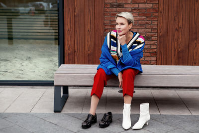 Street style. adult woman sitting and thinking, choosing which shoes to wear, white boots or black