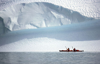 Two men rowing their sea kayak along an iceberg in greenland