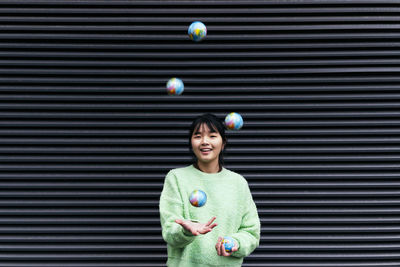 Woman juggling with globe balls in front of black corrugated wall