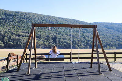 Rear view of woman sitting on swing against mountain