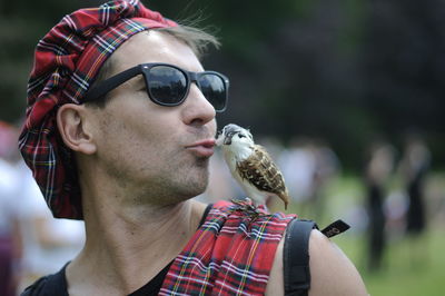 Close-up of mature man wearing sunglasses kissing bird sitting on shoulder