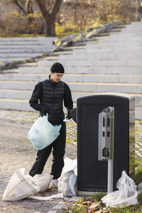 Male environmentalist with plastic waste standing by garbage can