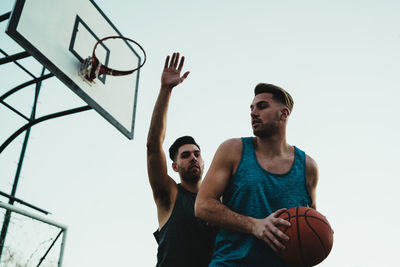 Low angle view of men playing basketball against clear sky