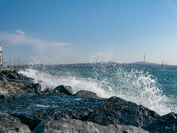 Sea waves splashing on rocks against blue sky