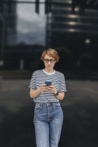 Woman using smart phone standing in front of black wall