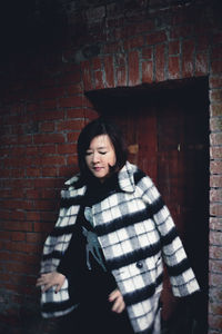 Portrait of smiling young woman standing against brick wall