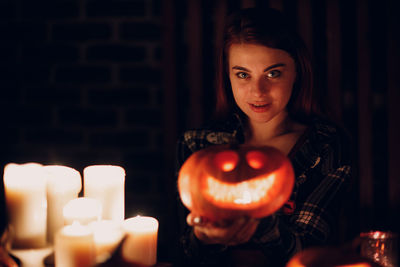 Portrait of young woman standing by illuminated lantern