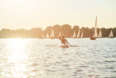 Mid adult woman canoeing on sea against clear sky during sunset