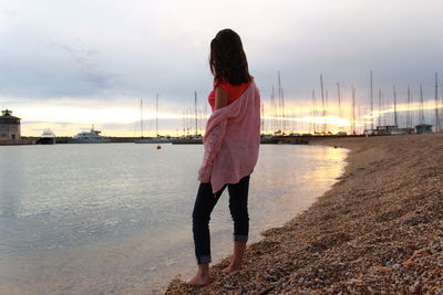 Rear view full length of woman standing at harbor against cloudy sky