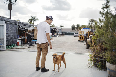 Rear view of carpenter with dog standing outside workshop against sky