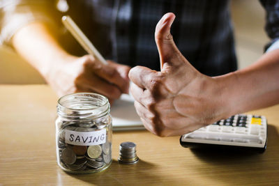 Close-up of hand holding coins in jar on table