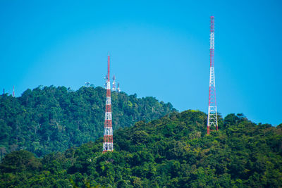 Low angle view of communications tower and trees against clear blue sky