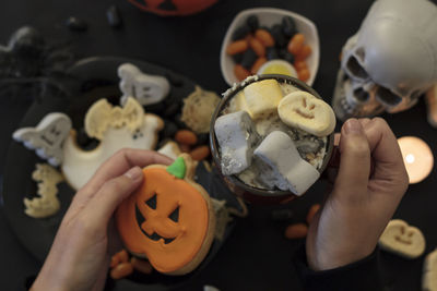 Top view of woman eating a pumpkin cookie and drinking spooky drink on table