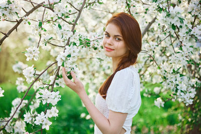 Portrait of young woman standing against tree