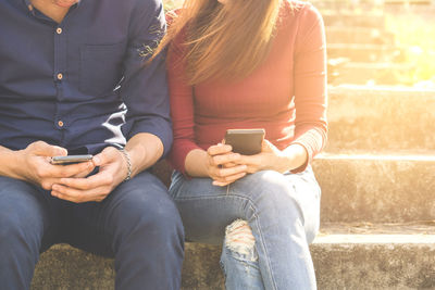 Midsection of couple using mobile phones on steps