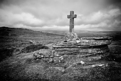 Low angle view of cross on rock against cloudy sky