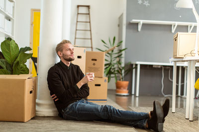 Full length of thoughtful young businessman with coffee cup sitting on floor at creative office