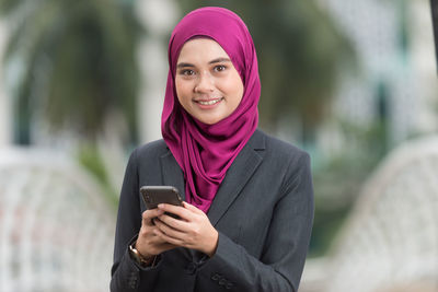 Portrait of a smiling young woman using mobile phone outdoors