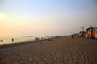 People enjoying at beach against clear sky during sunset
