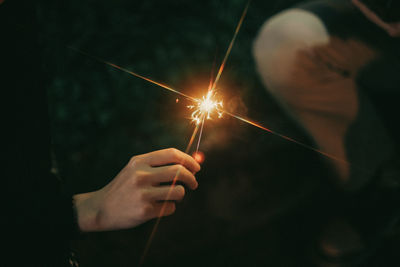 Cropped hand holding sparkler at night