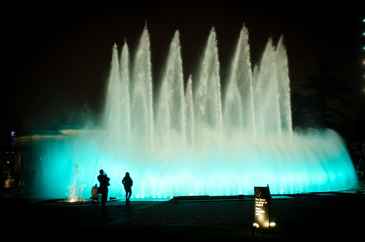 PANORAMIC VIEW OF SILHOUETTE MAN STANDING AGAINST ILLUMINATED FOUNTAIN