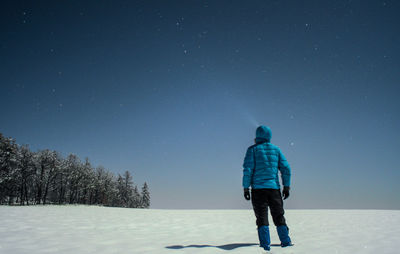 Rear view of man standing on snow against sky at night