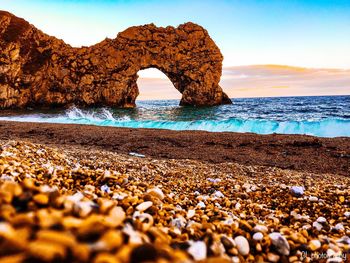 Rocks on beach against sky during sunset