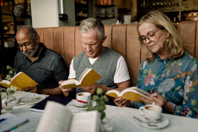 Senior men and woman reading books while sitting in cafe