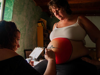 Woman painting on pregnant friend belly