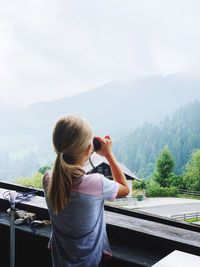 Rear view of woman photographing on mountain against sky