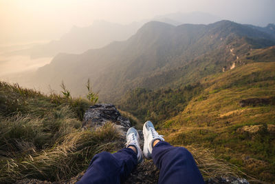 Low section of person relaxing on mountain during sunset