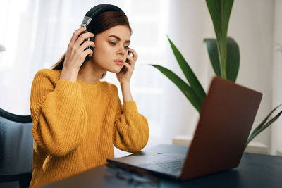 Young woman wearing headphones while using laptop