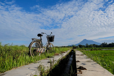 Bicycle on footpath by road against sky