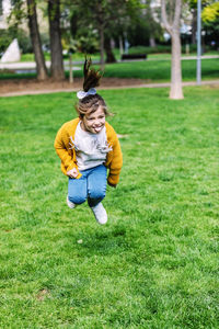 Happy cute girl sticking out tongue while jumping on grassy field in park
