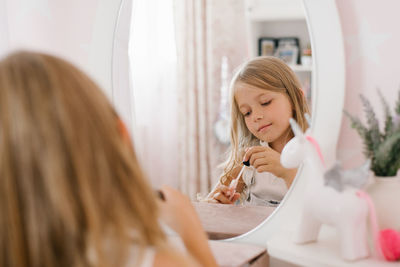 Pretty child girl paints her lips with glitter or balm in front of a mirror in her room