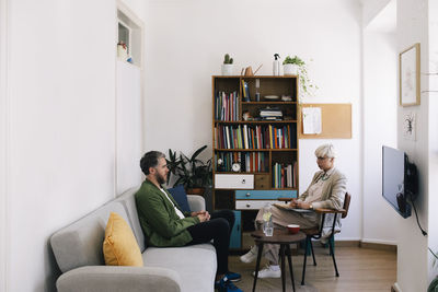 Female psychotherapist talking with male patient sitting on sofa at therapy office