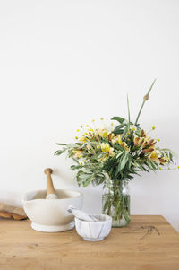 Mortar and pestle by flowers in vase on table by wall