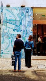 Rear view of people standing against graffiti in city