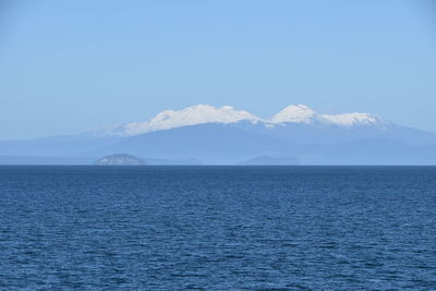 Scenic view of sea and mountains against clear blue sky